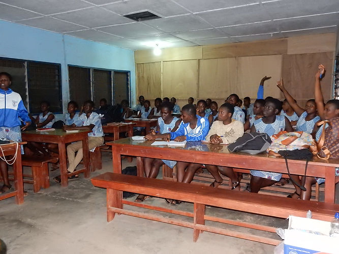 Classroom of students in blue uniforms, raising hands, and attending a lecture. Projects Abroad Foun.