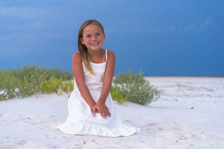 A teen sits at the edge of vibrant colored sand dunes during blue hour on St. George Island.