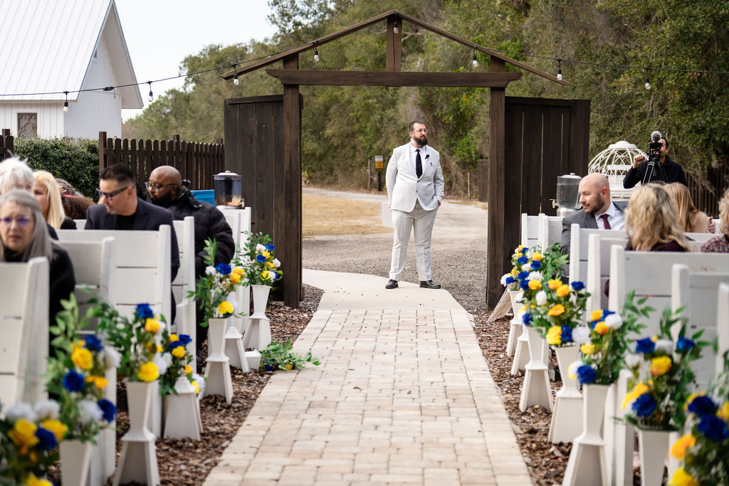 Man standing at the entrance to a flower-lined wedding aisle