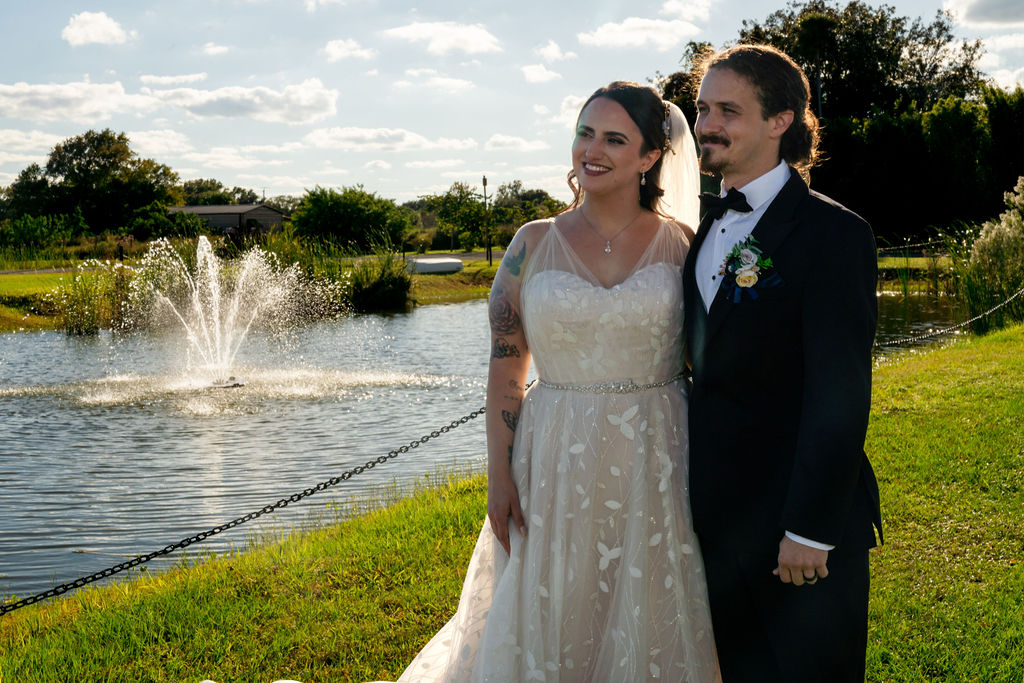 Bride and groom smiling beside a pond fountain