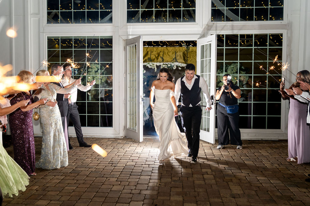 Bride and groom emerging through venue doors beneath raised sparklers