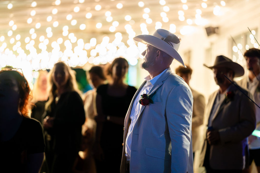 Groom standing beneath a canopy of glowing string lights