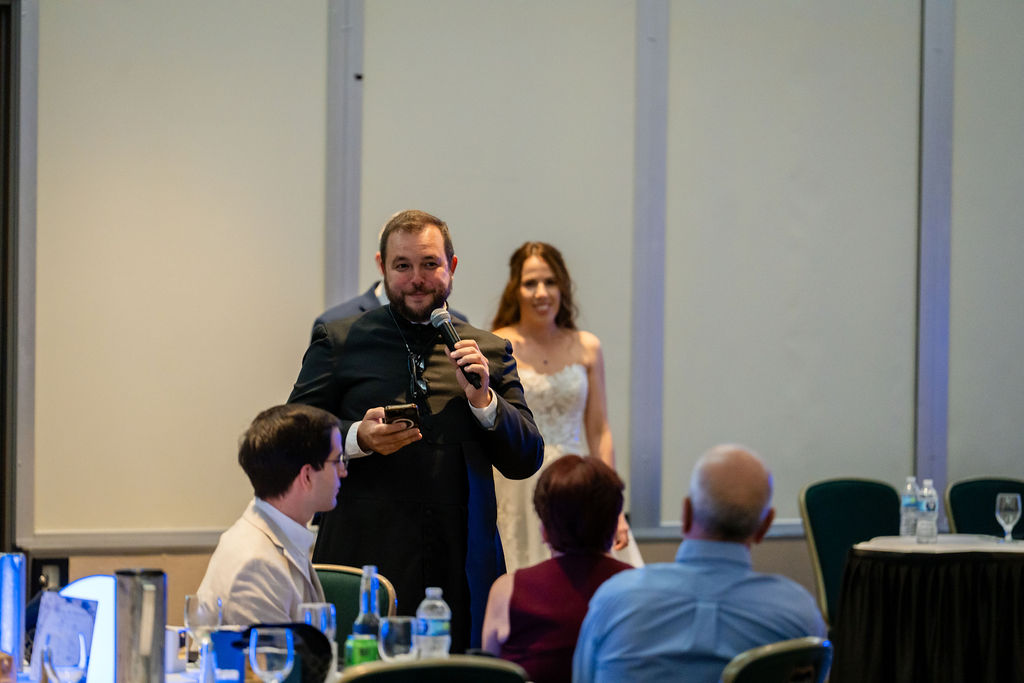 Wedding speaker addressing guests with the bride behind him