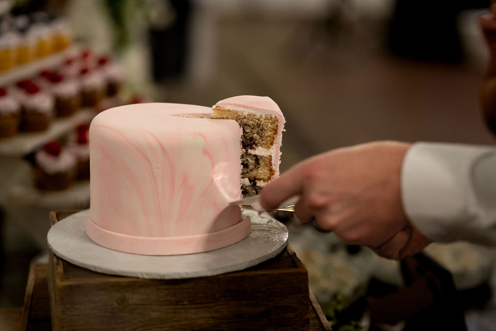 Close-up of a slice being cut from a small pink wedding cake