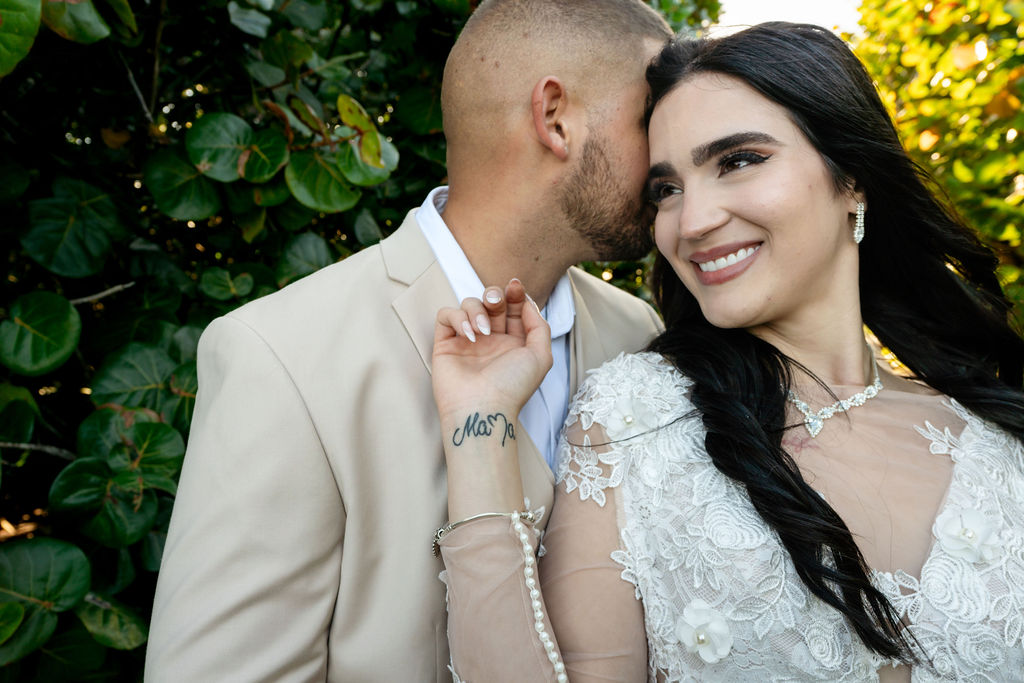 Groom leaning close while the bride smiles in coastal greenery