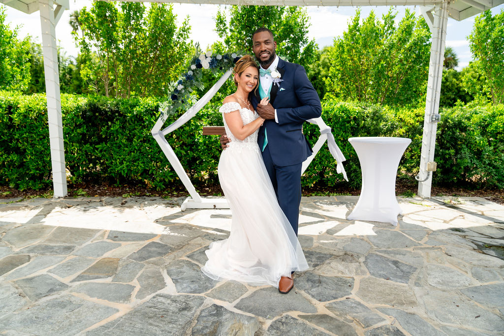 Bride and groom posing playfully beneath a floral ceremony arch