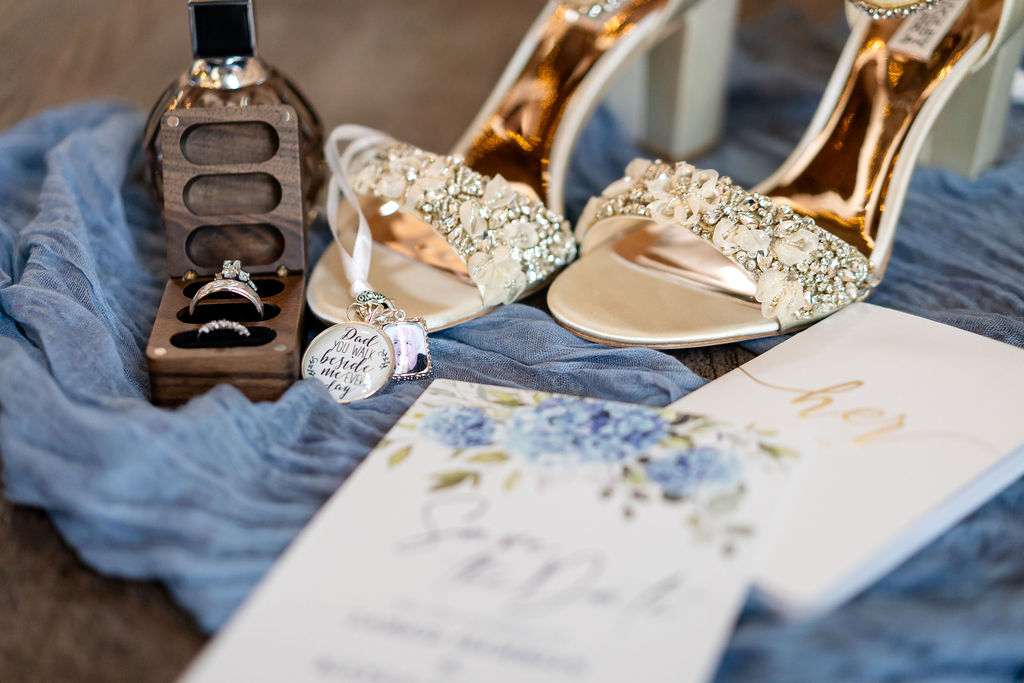 Bride’s sparkling wedding shoes and jewelry arranged on blue fabric
