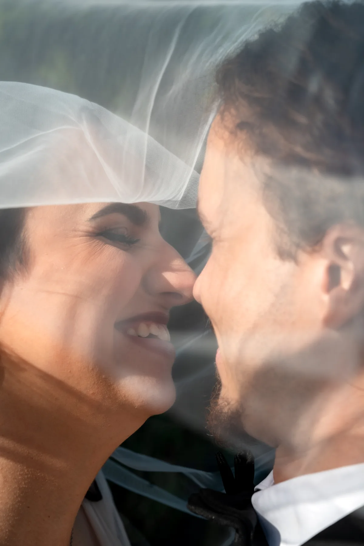 Bride and groom smiling closely through veil with soft natural light and intimate framing