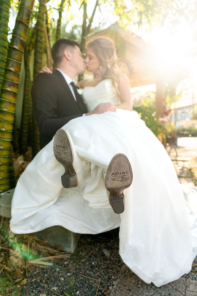 Groom holding the bride as they kiss among bamboo in glowing sunlight