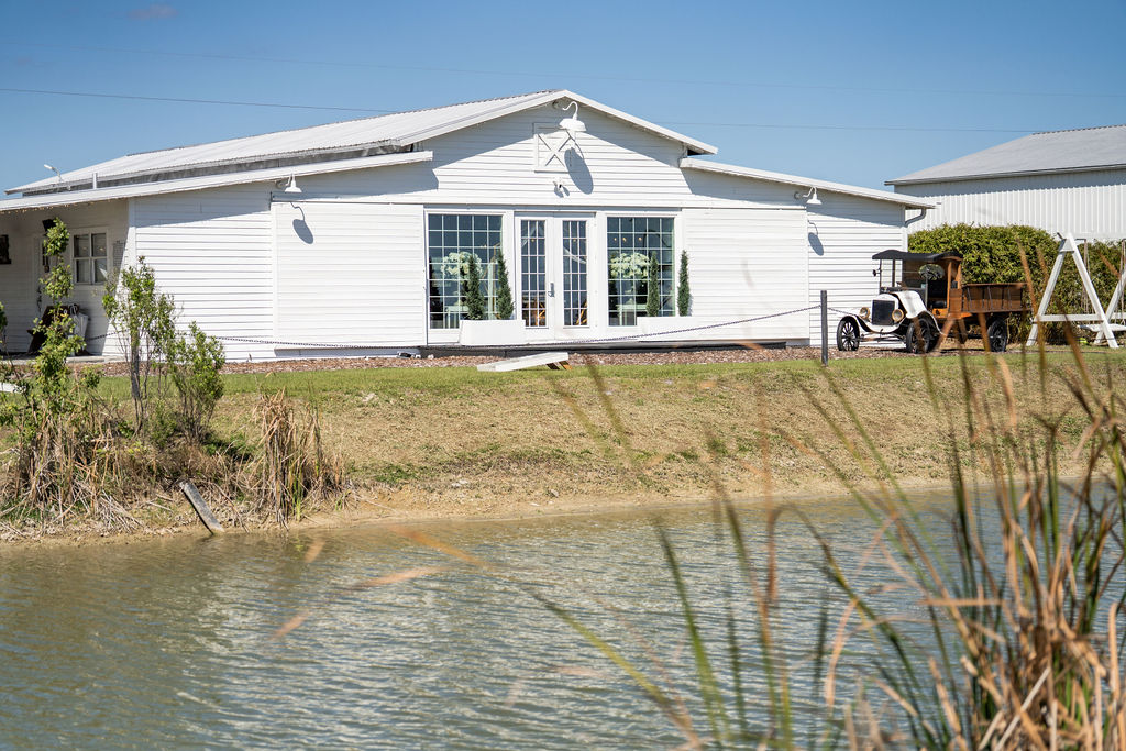 White wedding barn reflected across a pond edged with grasses