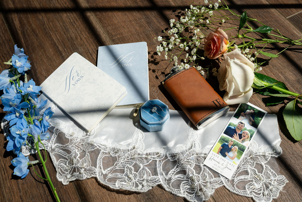 Wedding stationery, rings, perfume and flowers arranged on lace and wood