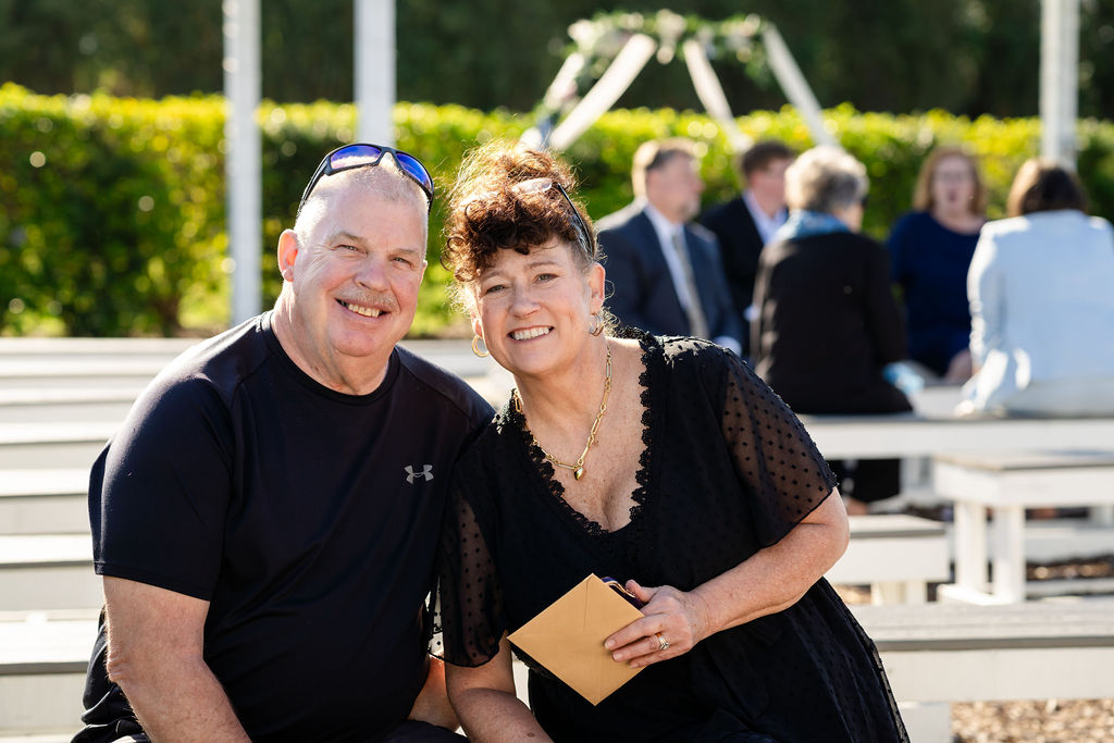 Two smiling adult guests posing at the outdoor wedding venue