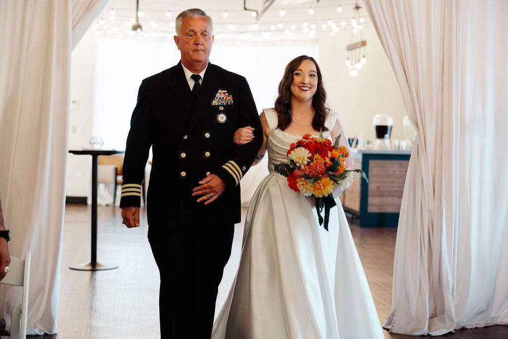 Bride walking down the aisle beside an older loved one in formal uniform