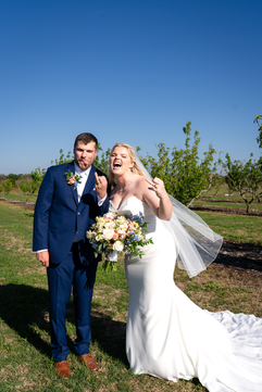 Bride and groom posing playfully outdoors in bright natural light holding bouquet and smiling