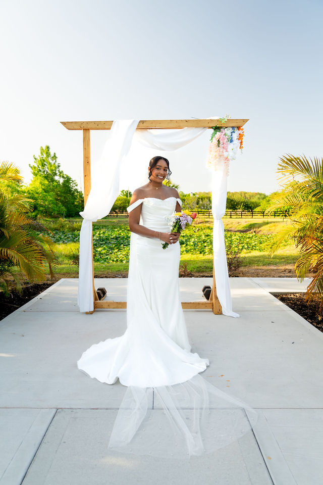 Bride holding a colorful bouquet beneath an outdoor wedding arch