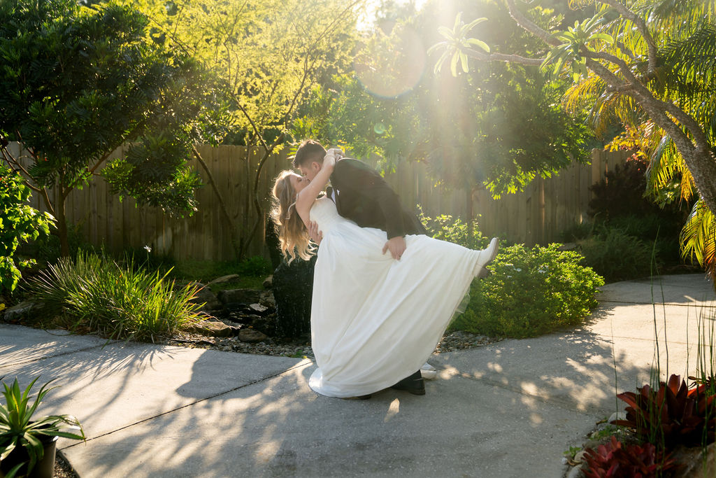 Groom dipping the bride in warm late-afternoon garden sunlight