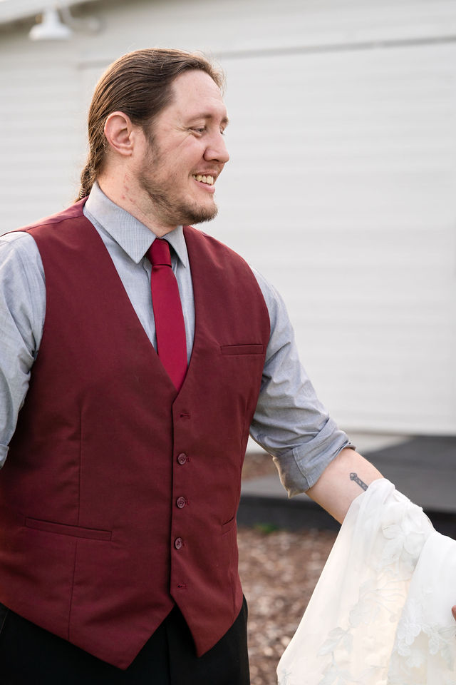 Groom smiling in a burgundy vest during wedding portraits