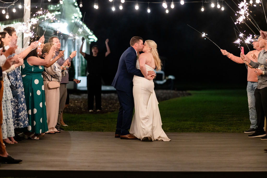 Bride and groom kissing as guests hold sparklers around them