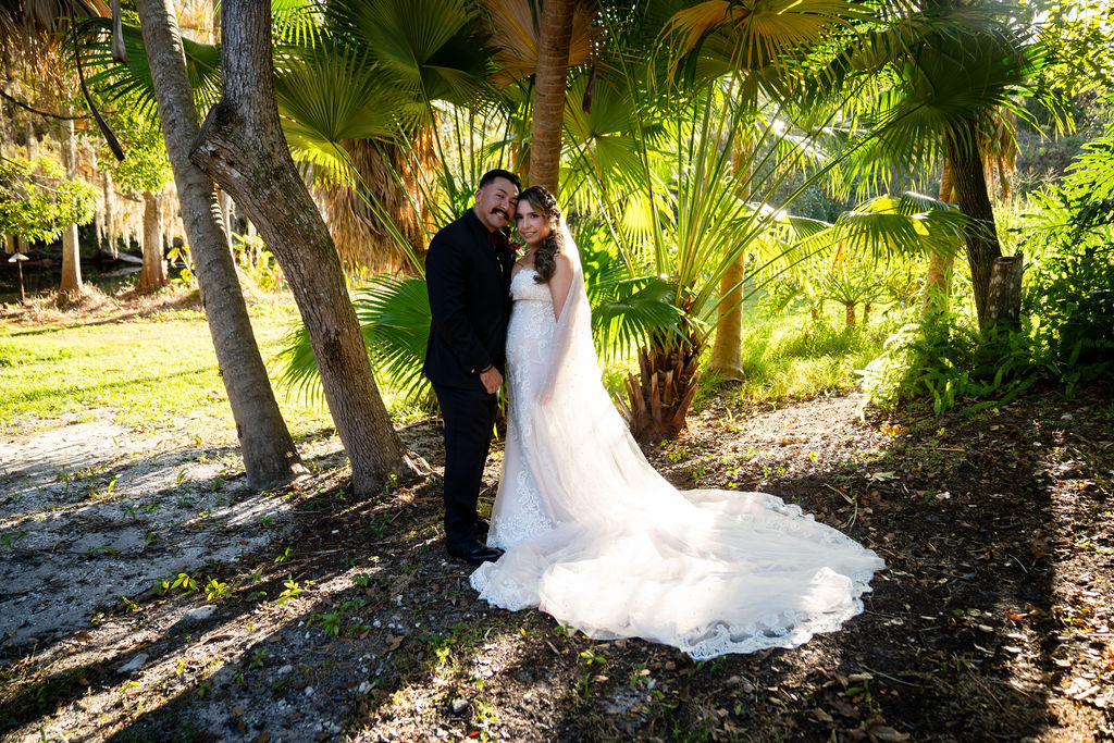Bride and groom kissing beneath palms with the dress train on the ground