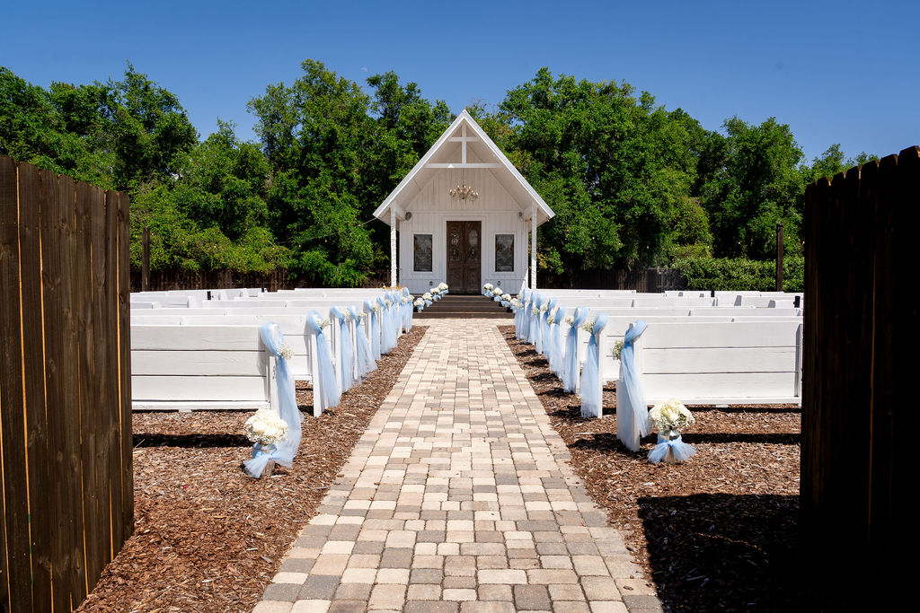 Wedding ceremony aisle leading between white pews to a small white chapel