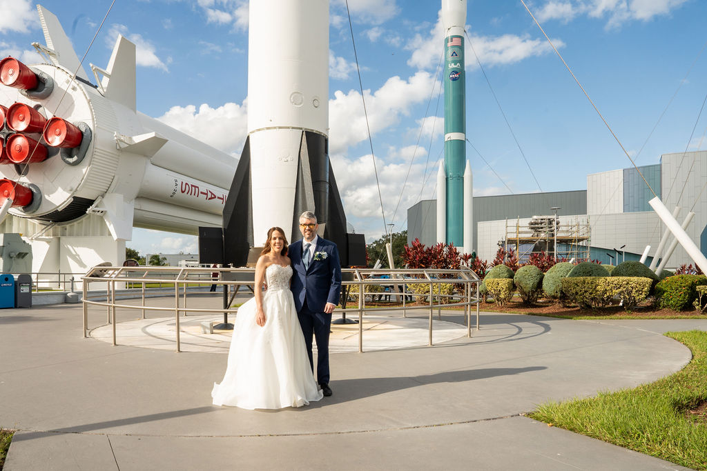 Wide wedding portrait of the couple among towering rocket exhibits