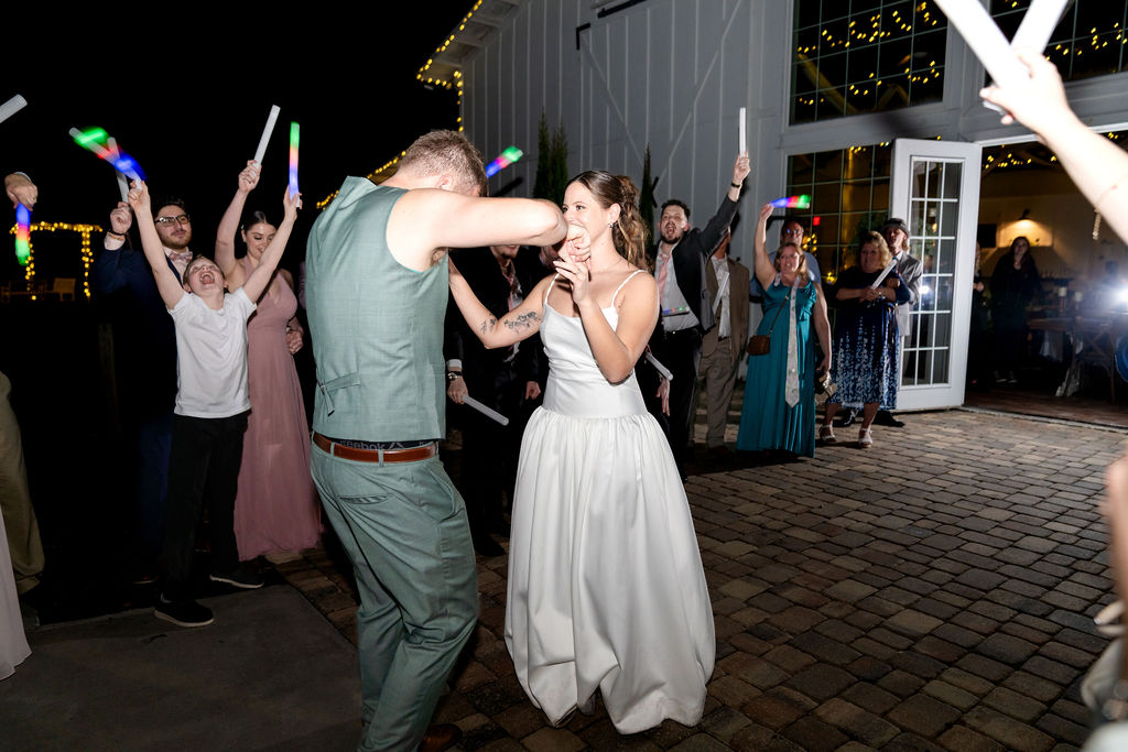 Bride and groom dancing outside as guests wave glow sticks