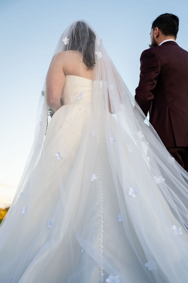 Back view of the bride’s veil and dress as she stands beside the groom