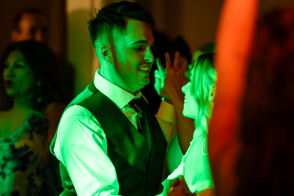 Groom under colorful green light on the reception dance floor