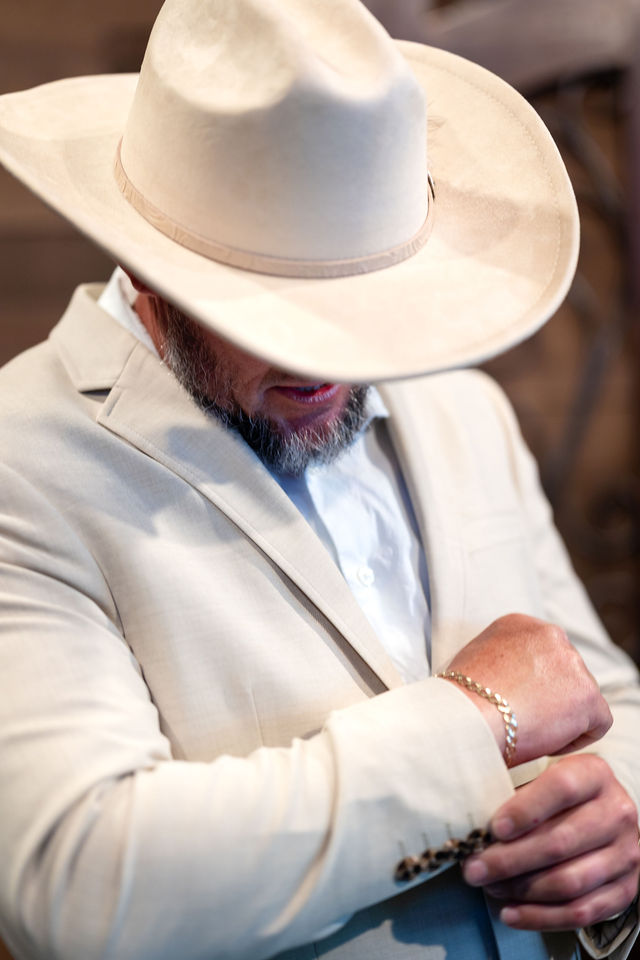 Groom in a cream jacket and cowboy hat adjusting his cuff