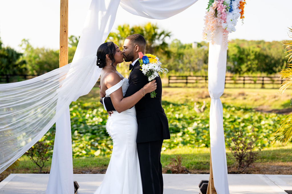 Bride and groom kissing beneath a flowing veil at their ceremony arch