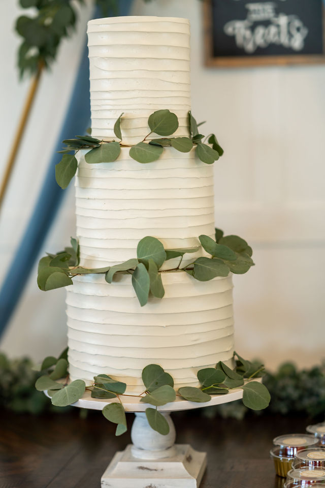 Three-tier white wedding cake decorated with greenery