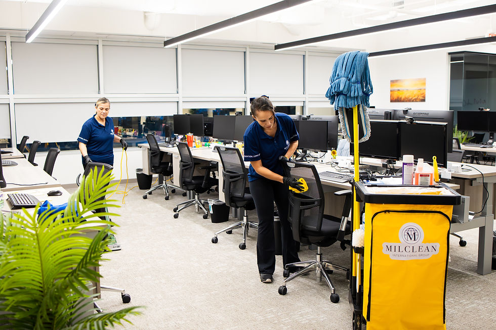 Two cleaners work among office desks, one wiping a chair beside a MilClean supply cart.
