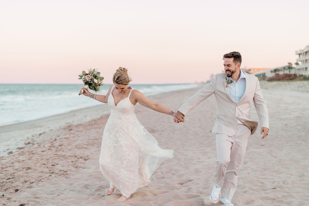 Bride and groom holding hands on the beach at sunset