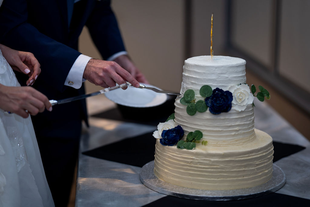 Close-up of newlyweds cutting a tiered cake with blue flowers