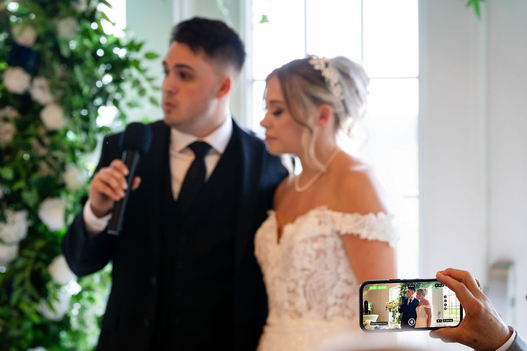Groom speaking into a microphone beside the bride
