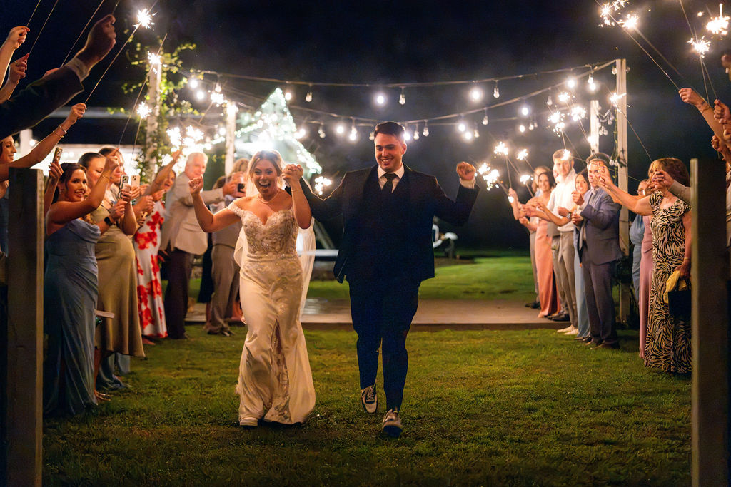 Bride and groom walking through a sparkler exit as guests cheer