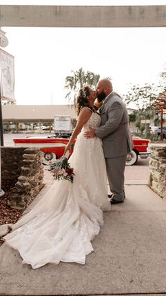 Bride and groom embracing outdoors near a vintage car during wedding day
