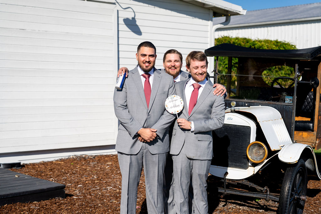 Three groomsmen posing beside a vintage wedding car