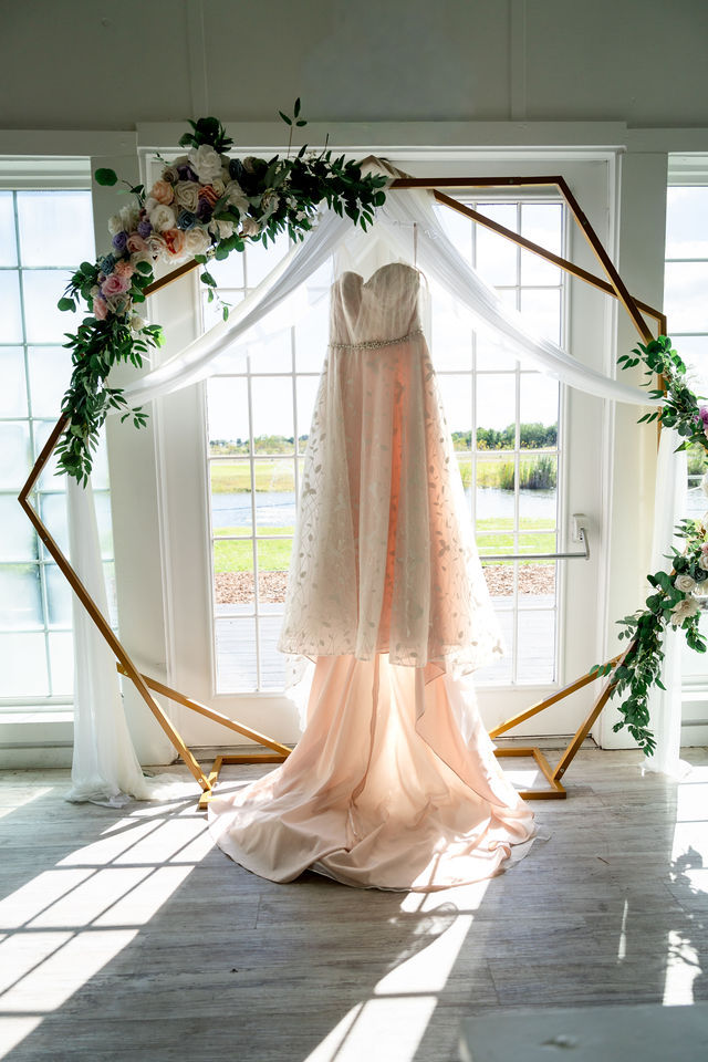 Blush wedding gown hanging in a floral ceremony arch