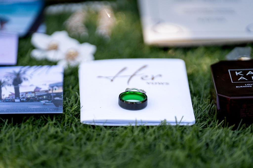 Green wedding band resting on a vow book in an outdoor flat lay
