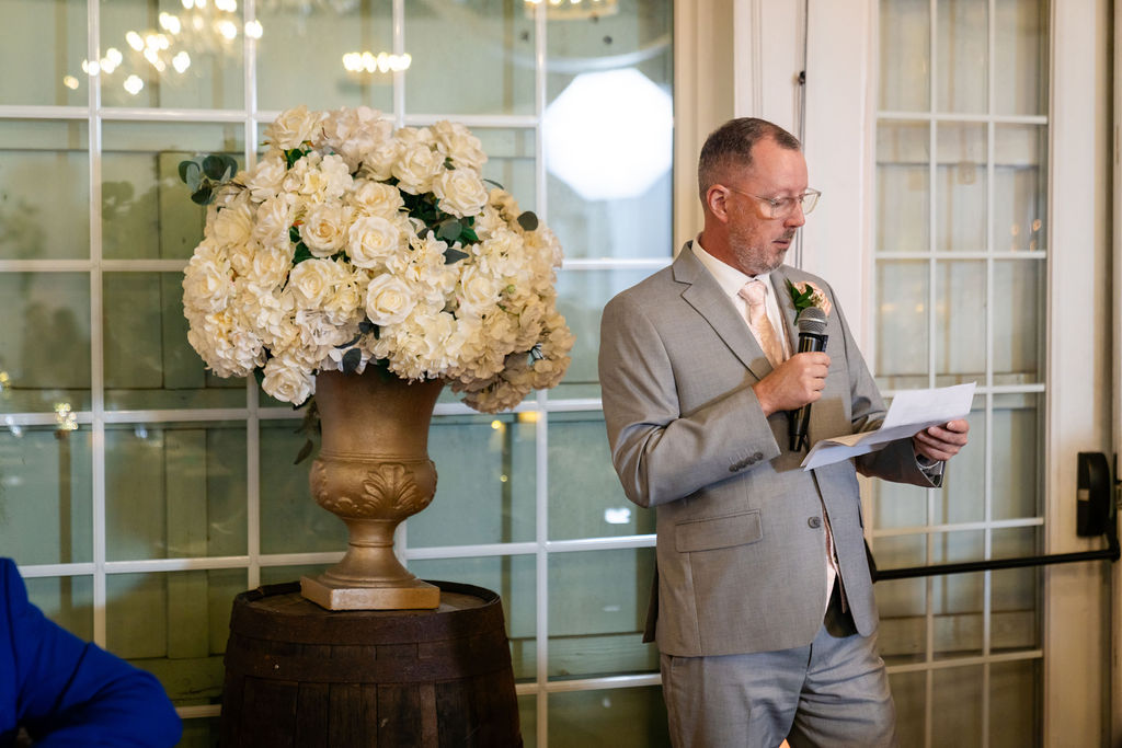 Bride’s father reading a wedding toast beside a floral arrangement