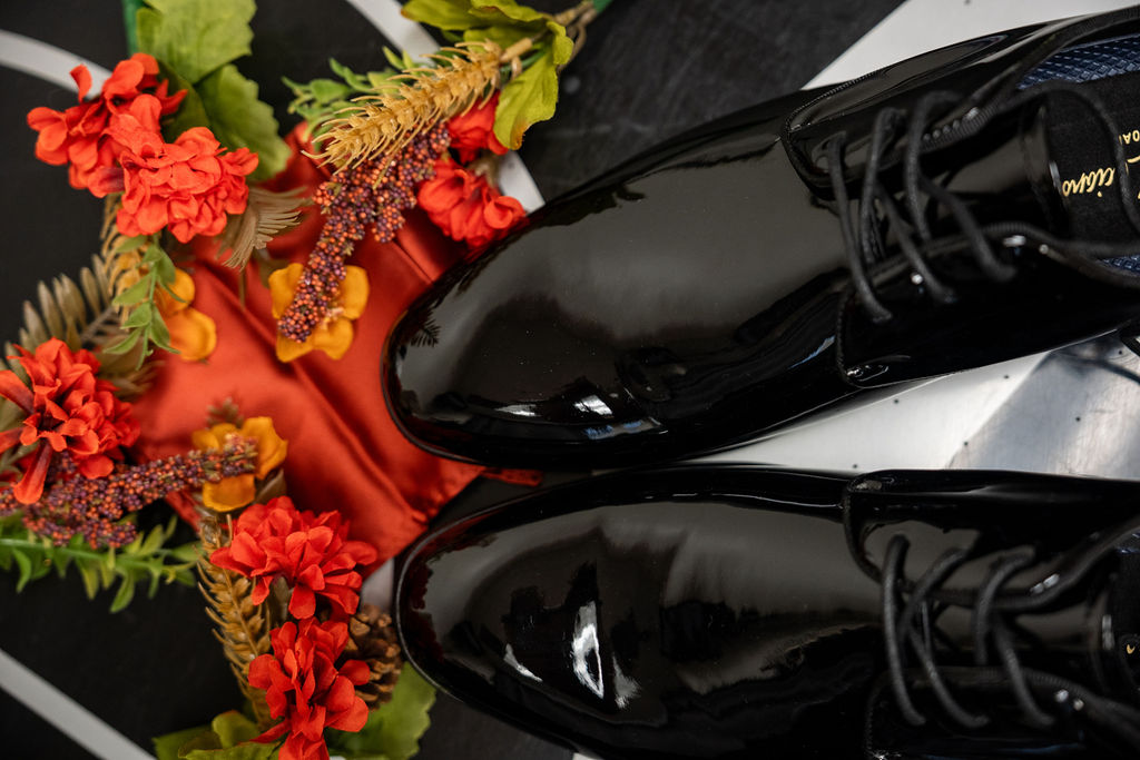 Groom’s polished black shoes beside orange floral wedding accessories