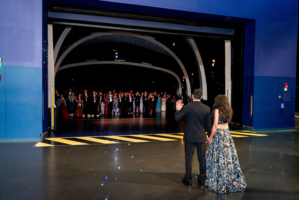 Bride and groom facing guests gathered in a dramatic curved hallway