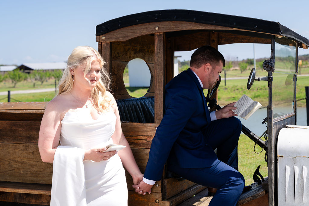 Bride and groom reading private vows beside a vintage car without seeing each other
