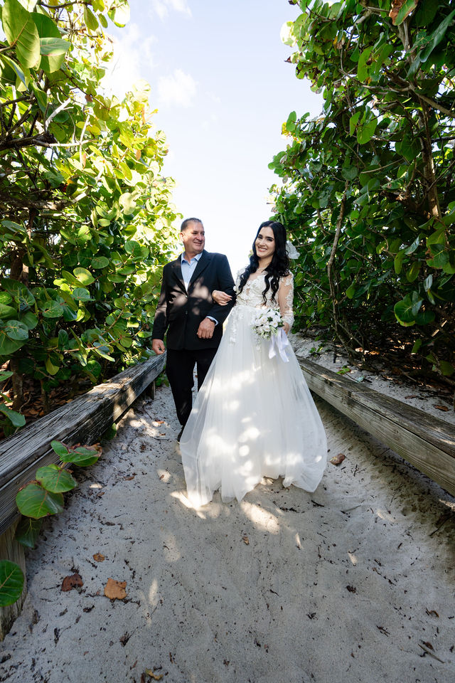 Bride posing with an adult man on a sunlit sandy path
