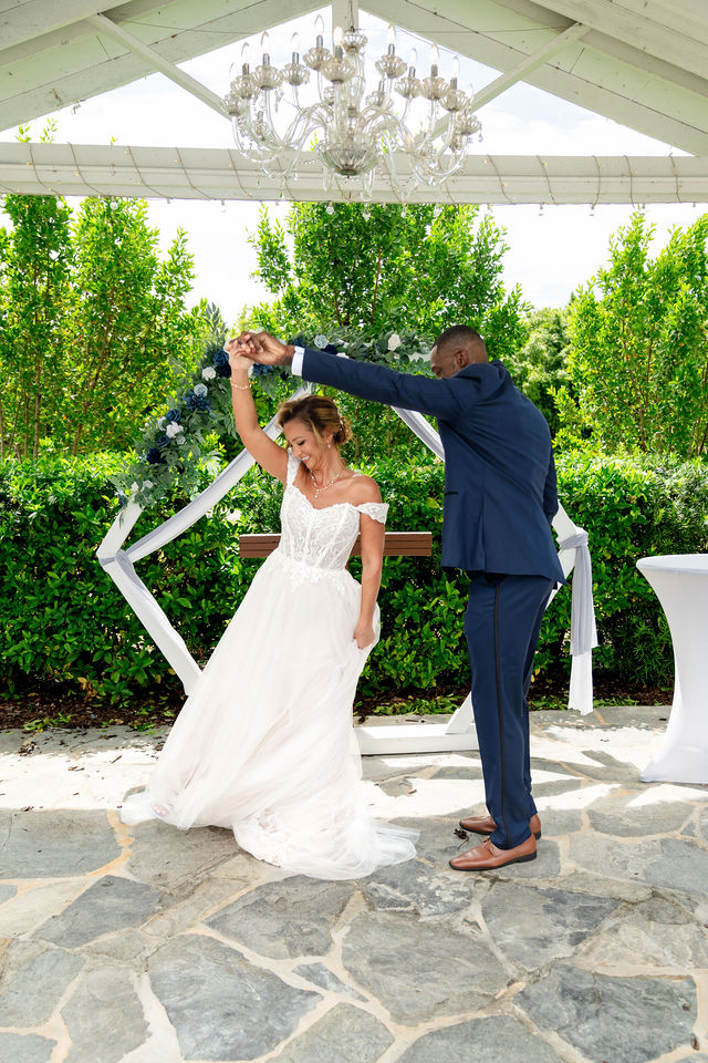 Groom twirling the bride beneath an outdoor pavilion