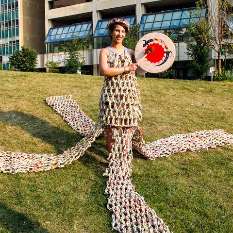 standing person wearing a newspaper dress on a hill and playing drum