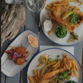 Fish and chips with peas, salad, and lemon on plates, restaurant food.