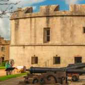 Historic cannons in front of a stone fort with a bright sky