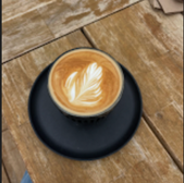 Latte art coffee in a black cup on a wooden table, close-up view.